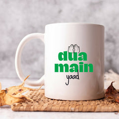 White ceramic mug featuring the phrase 'Dua Main Yaad' in elegant calligraphy. This spiritually meaningful design is perfect for those embarking on Umrah or Hajj, serving as a heartfelt reminder to be remembered in prayers. The mug is ideal for daily use, with a comfortable handle and ample capacity for hot or cold beverages, making it a thoughtful and cherished gift for loved ones during their spiritual journeys.